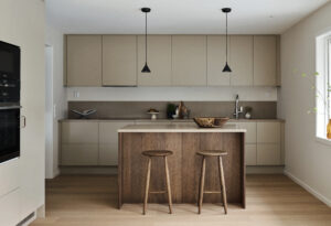 Ett kök i beige med köksö och två pallar i trä.